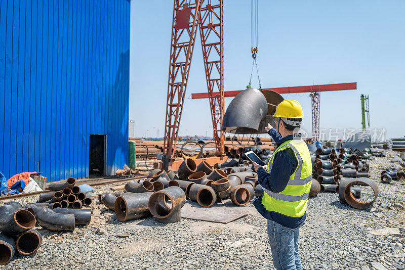 A middle-aged male worker watched the crane lift heavy objects on the construction site